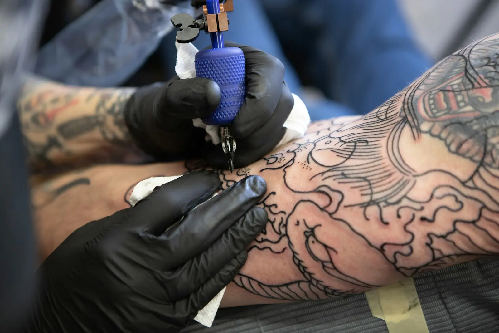 Tatuador con guantes negros trabajando sobre un brazo